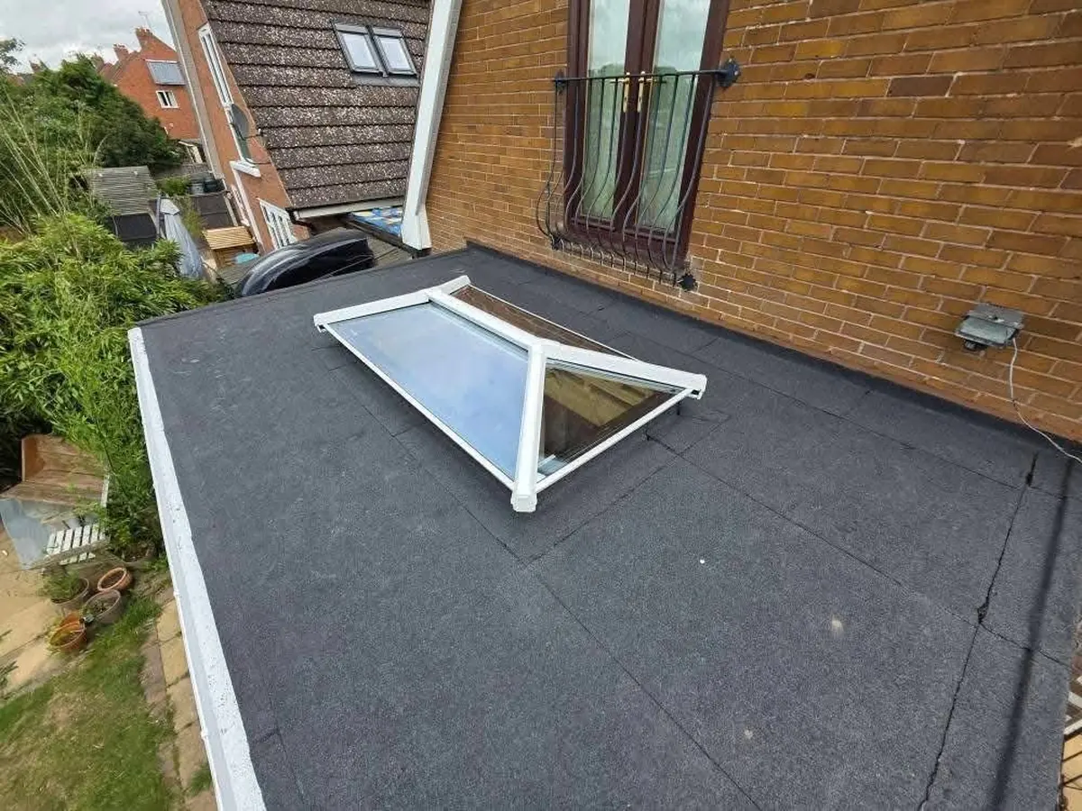 Side-angle view of felt flat roof installation with roof lantern and brick parapet