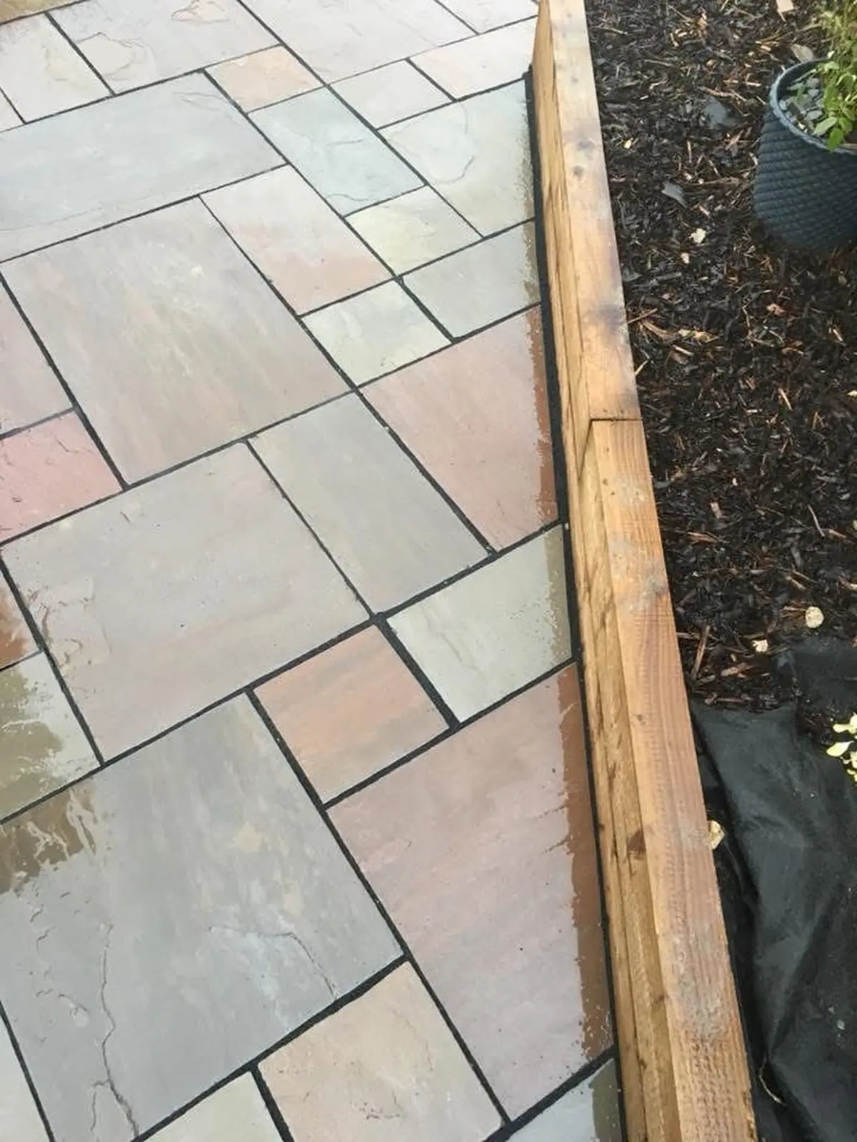 Close-up detail of sleeper edge meeting Indian sandstone slabs over weed-suppressant membrane