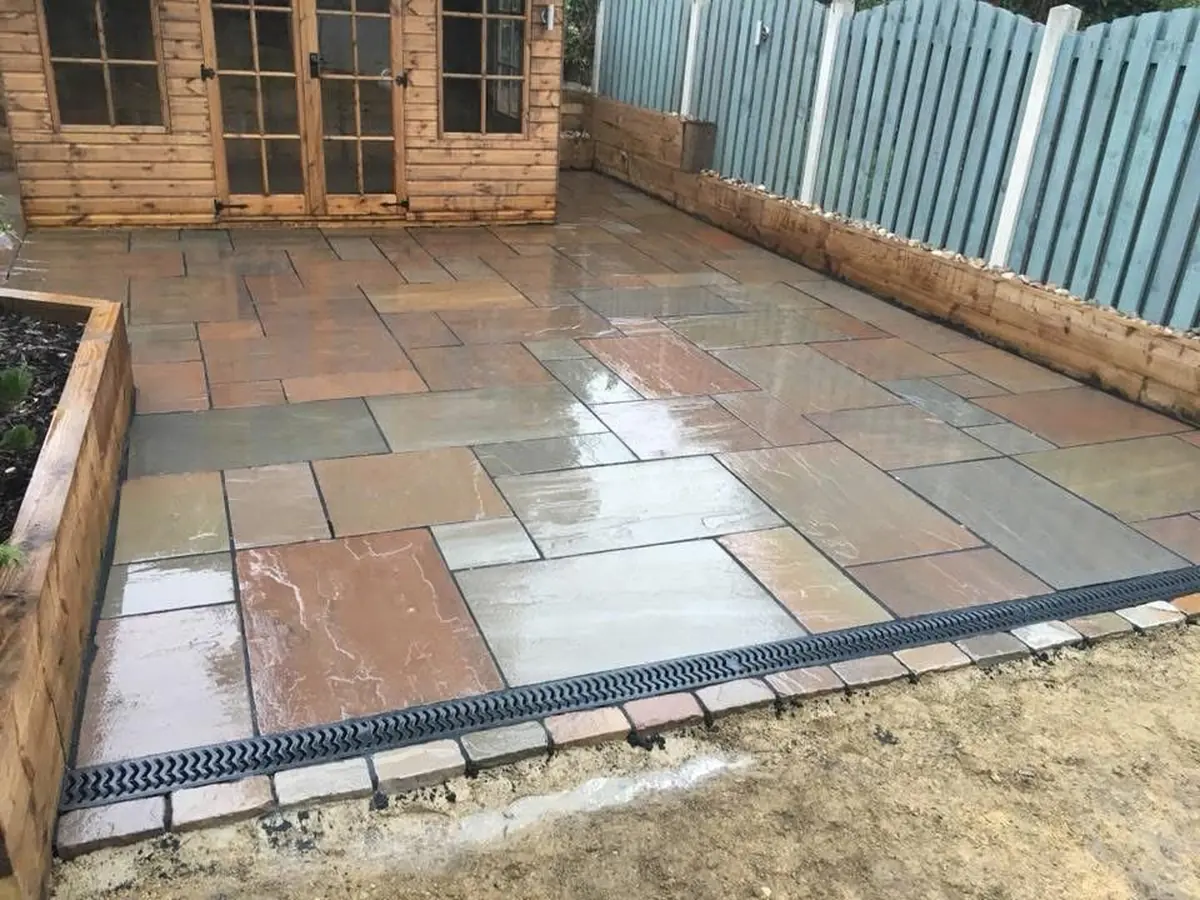 Indian sandstone patio laid in random pattern with summerhouse and ACO drainage channel