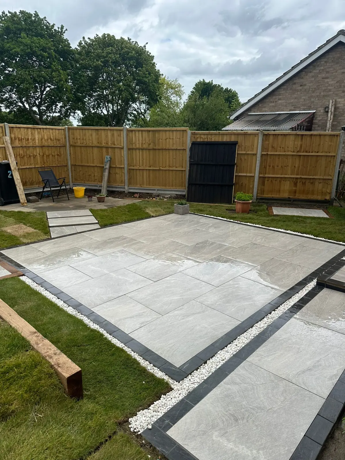 Grey porcelain paving patio with charcoal block-paving border and white pebble margin in a garden