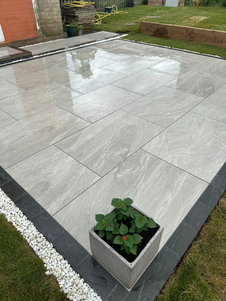 Close-up of grey porcelain paving with charcoal block-paving border and white gravel trim against the lawn