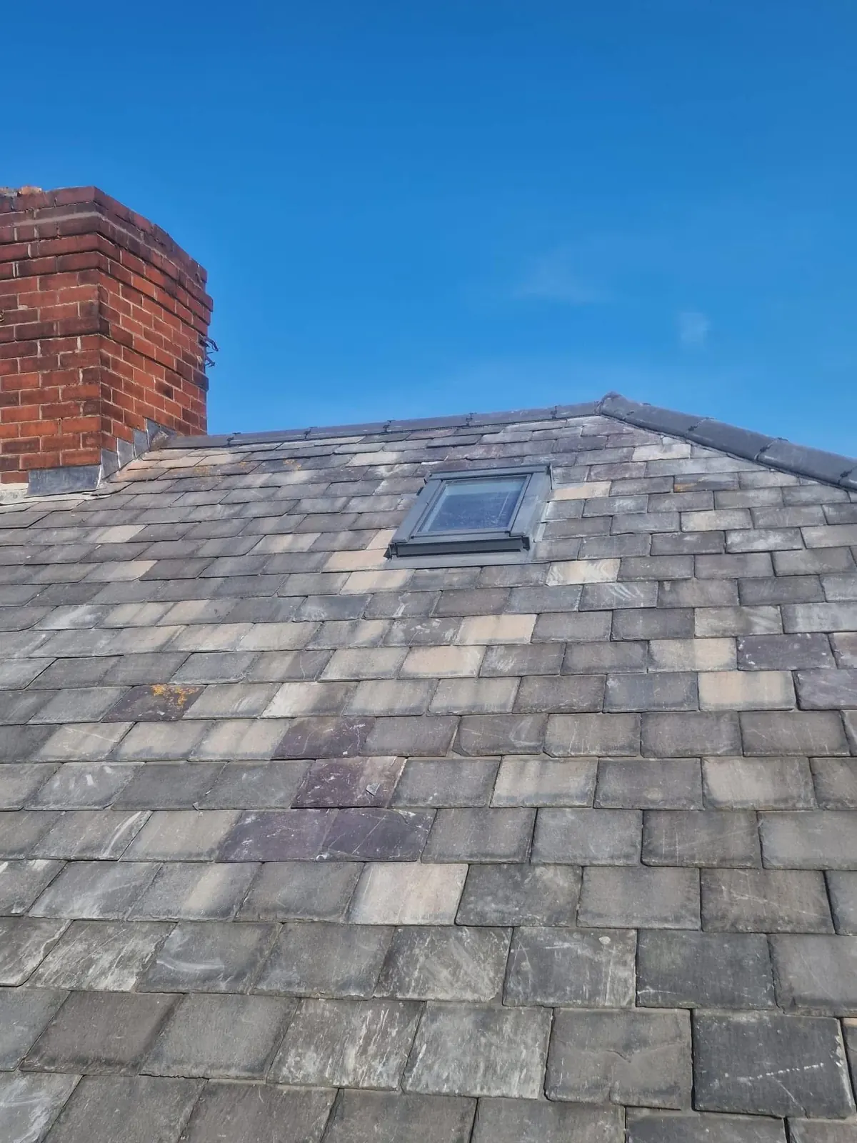 Close-up of a slate roof showing replacement slates, lead chimney flashing and roof window detail