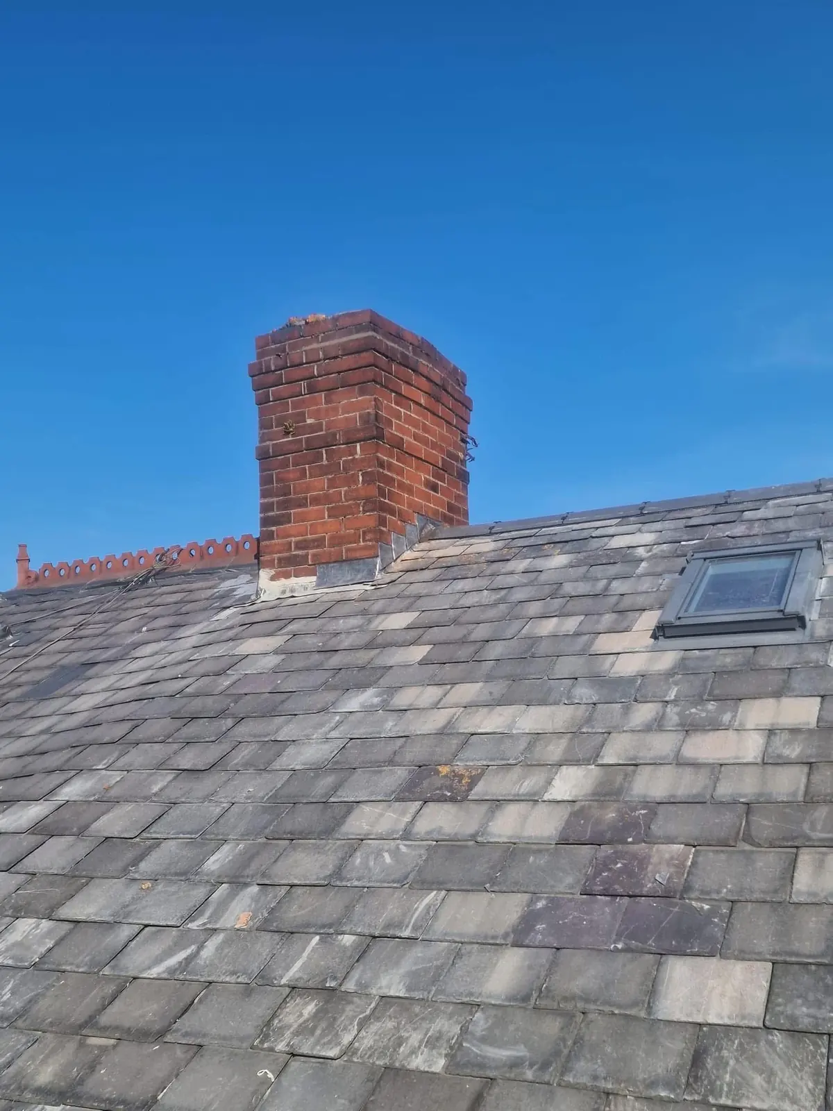 Restored slate roof with new Velux window and lead flashing around a tall brick chimney