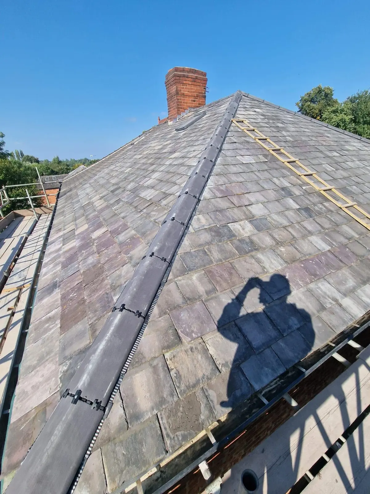 Slate roof restoration with new lead ridge, dry-verge system and re-laid Welsh slate around a brick chimney