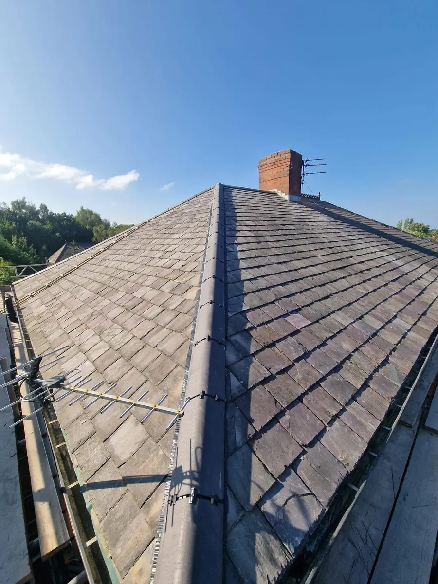 Full hipped slate roof viewed along the ridge with new lead ridge flashing leading to a brick chimney stack